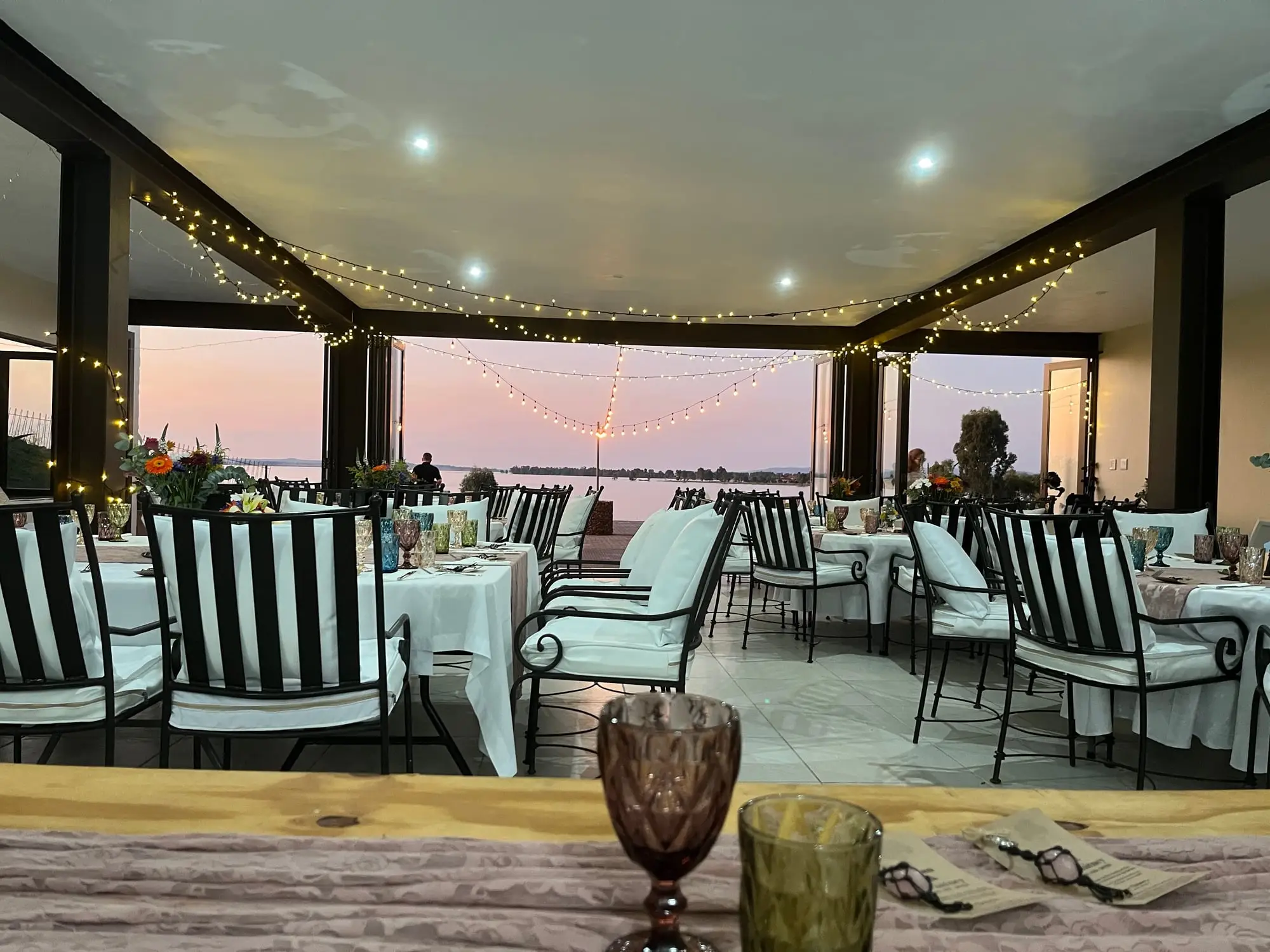 The downstairs venue set for dinner under festoon lights, looking out over the Vaal Dam
