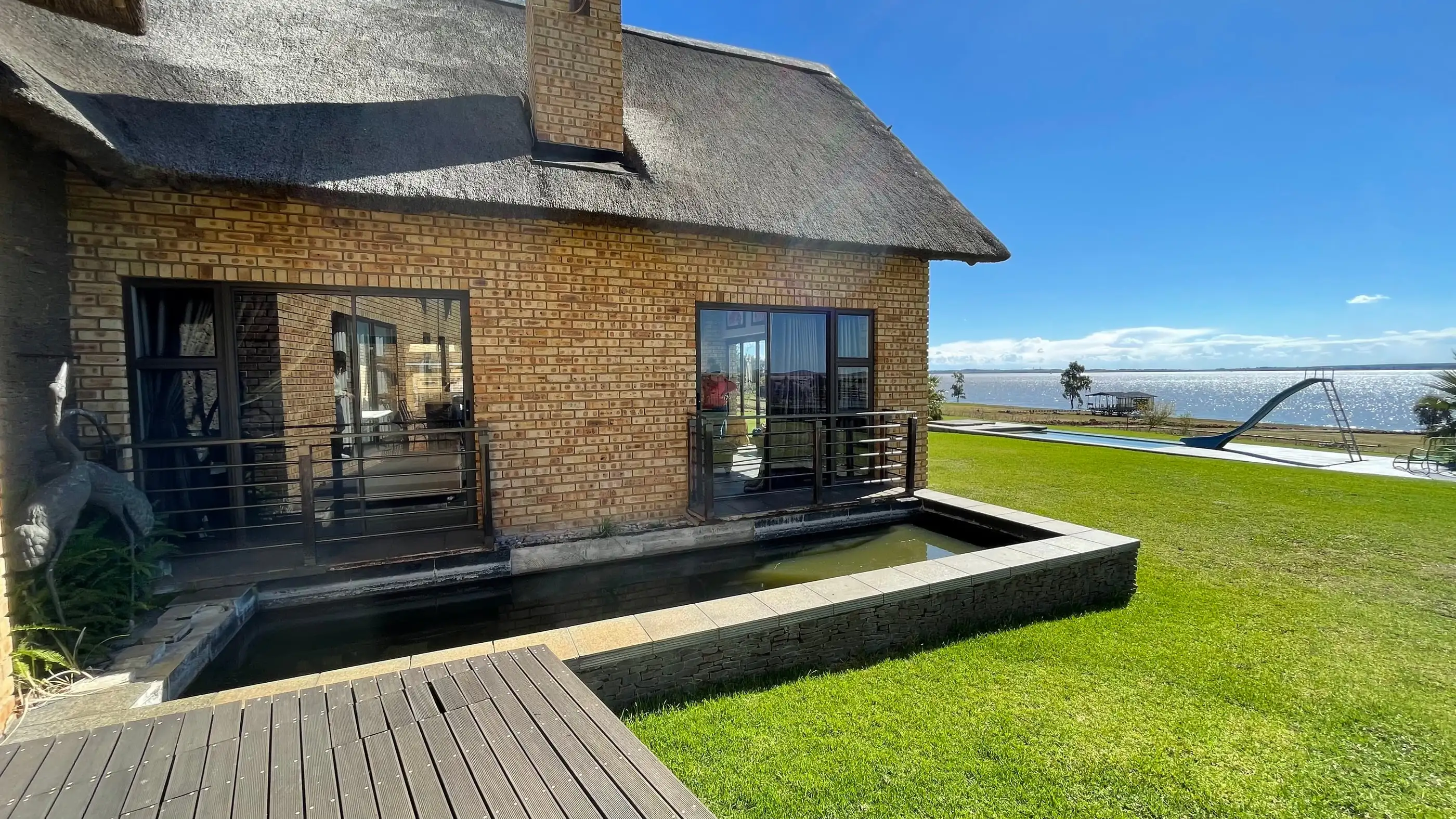 The thatched guesthouse on the lawn, with the pool and the Vaal Dam stretching out behind it